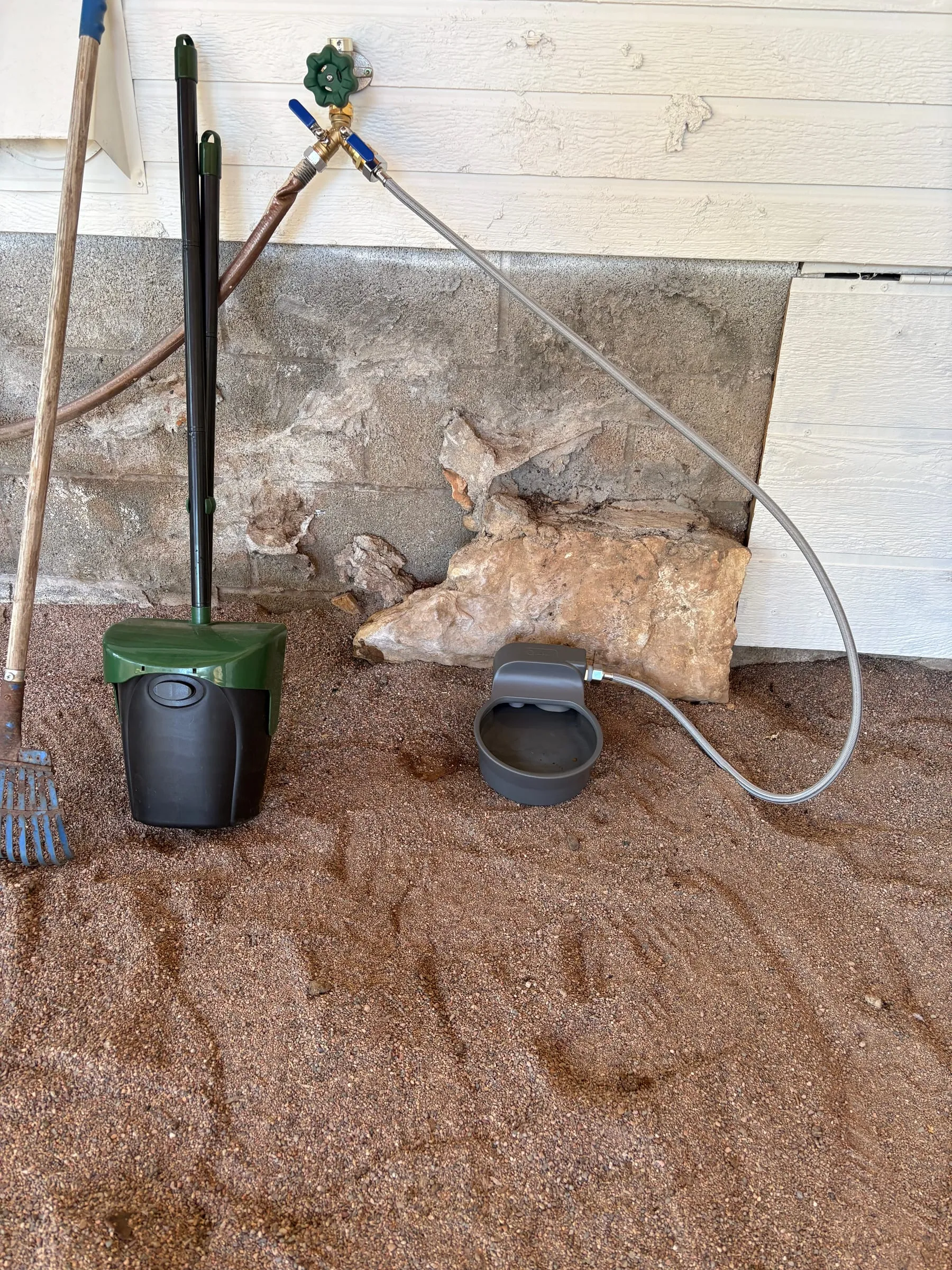 An automatic water bowl in the dog run, plumbed to a spigot on the wall by a braided line, so it refills itself as a dog drinks.