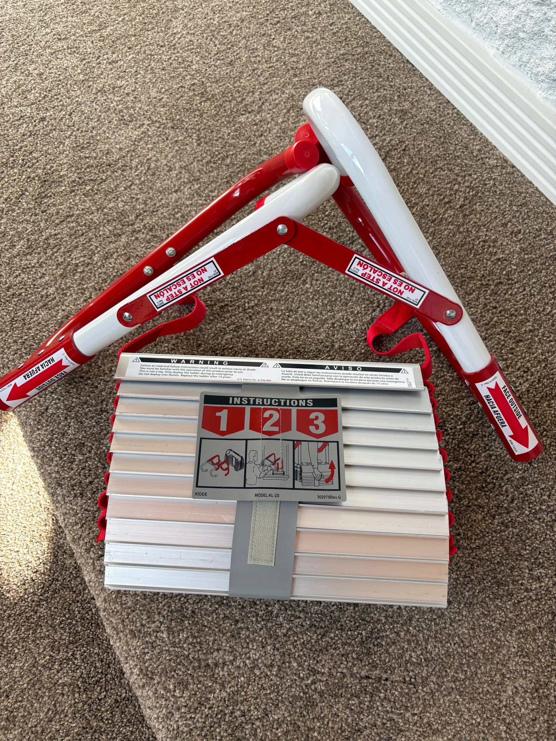 A folding emergency escape ladder on the floor, rungs banded together, with its hooks open and the printed instructions facing up.