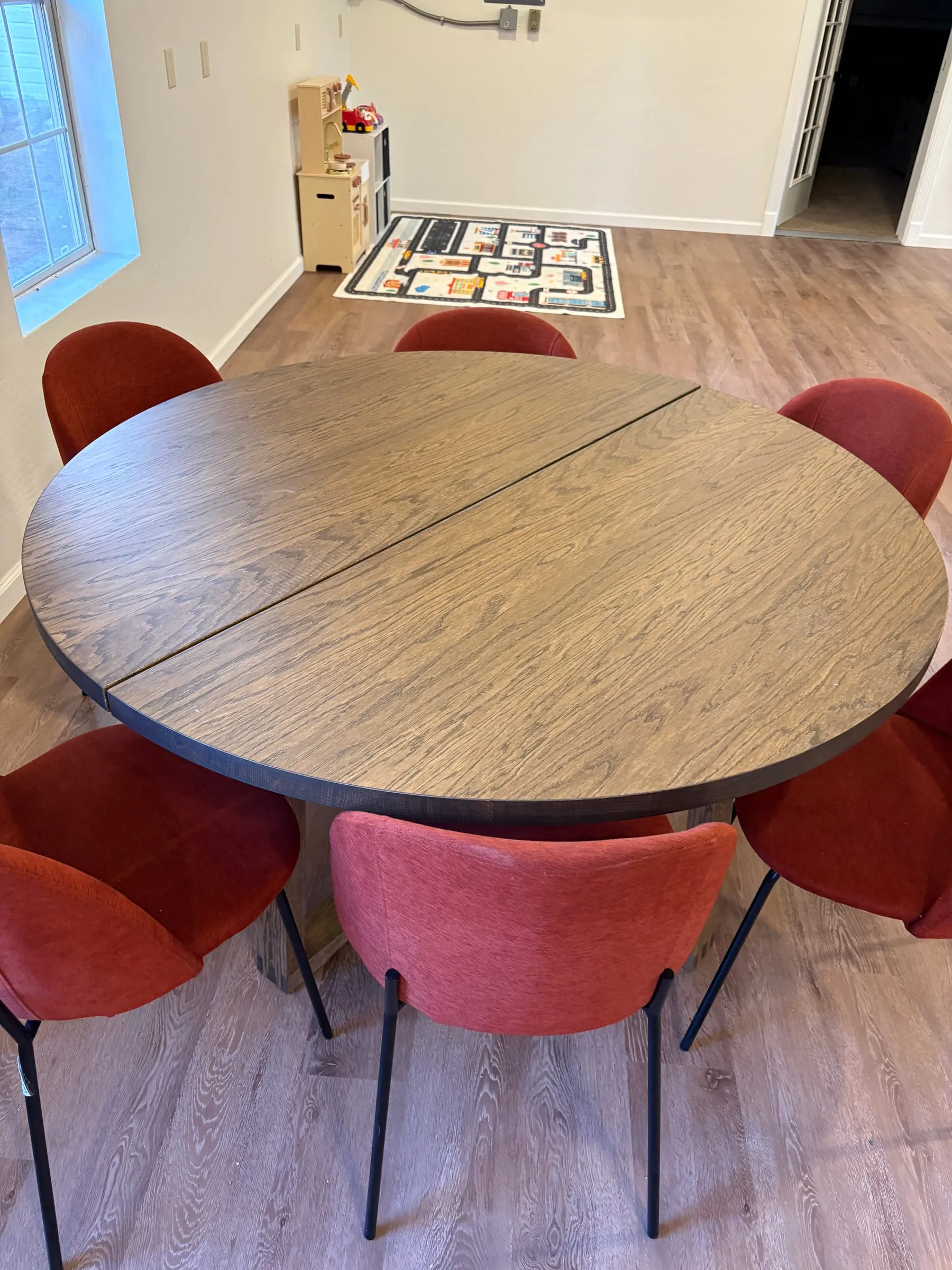 A round wood card table with six upholstered chairs around it, in the middle of the game room.