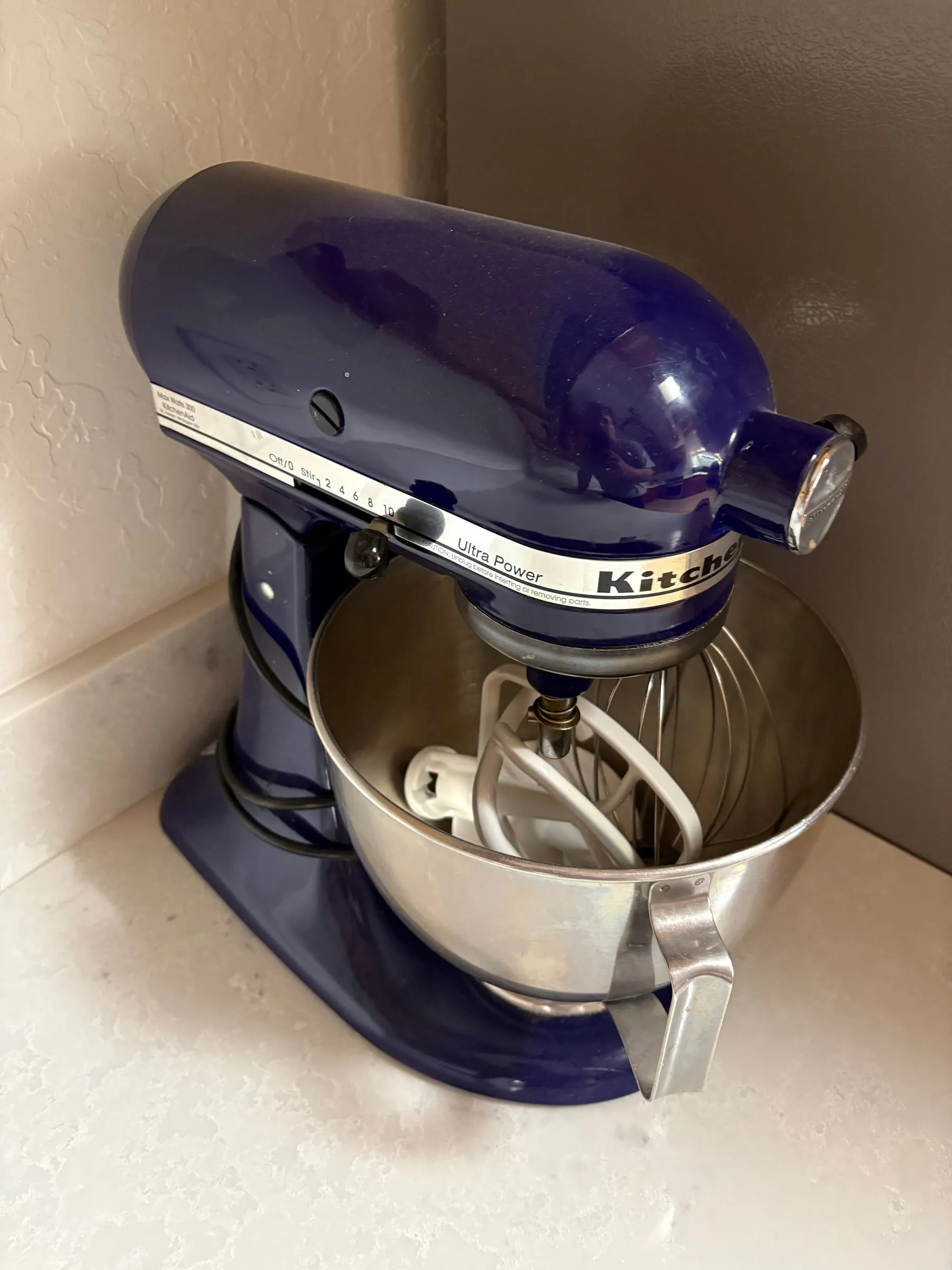 A blue KitchenAid stand mixer on the kitchen counter, with its stainless bowl and wire whisk attached.