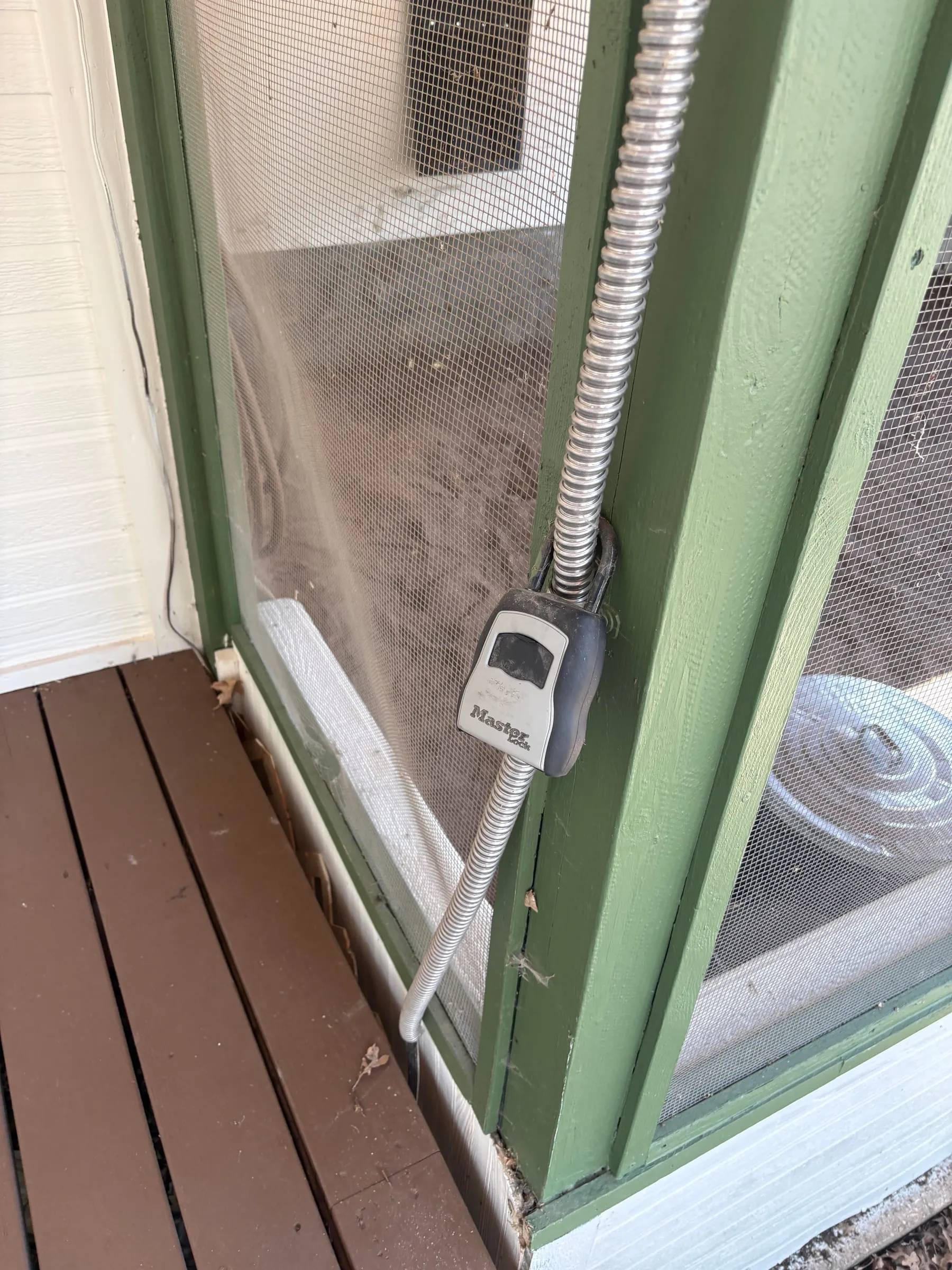 A combination lockbox hanging on the green wooden frame beside the dog run door, holding the spare keys.