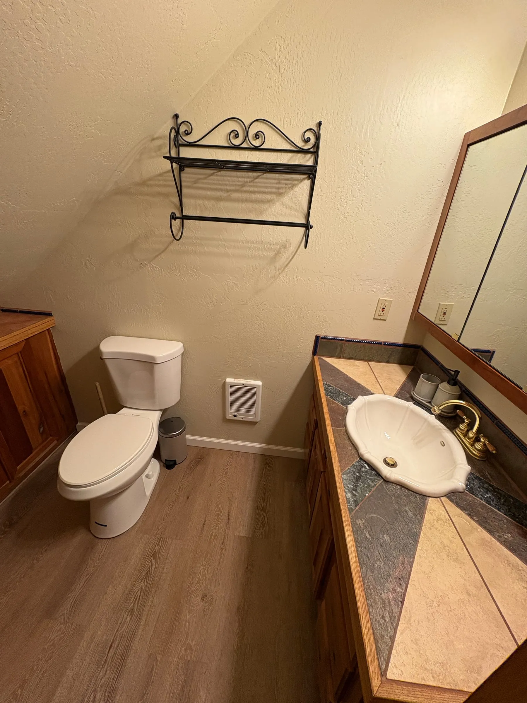 The vanity in the bathroom in Nora’s studio — a scalloped basin with brass taps on a tiled counter, a framed mirror above it, and a toilet beside it.