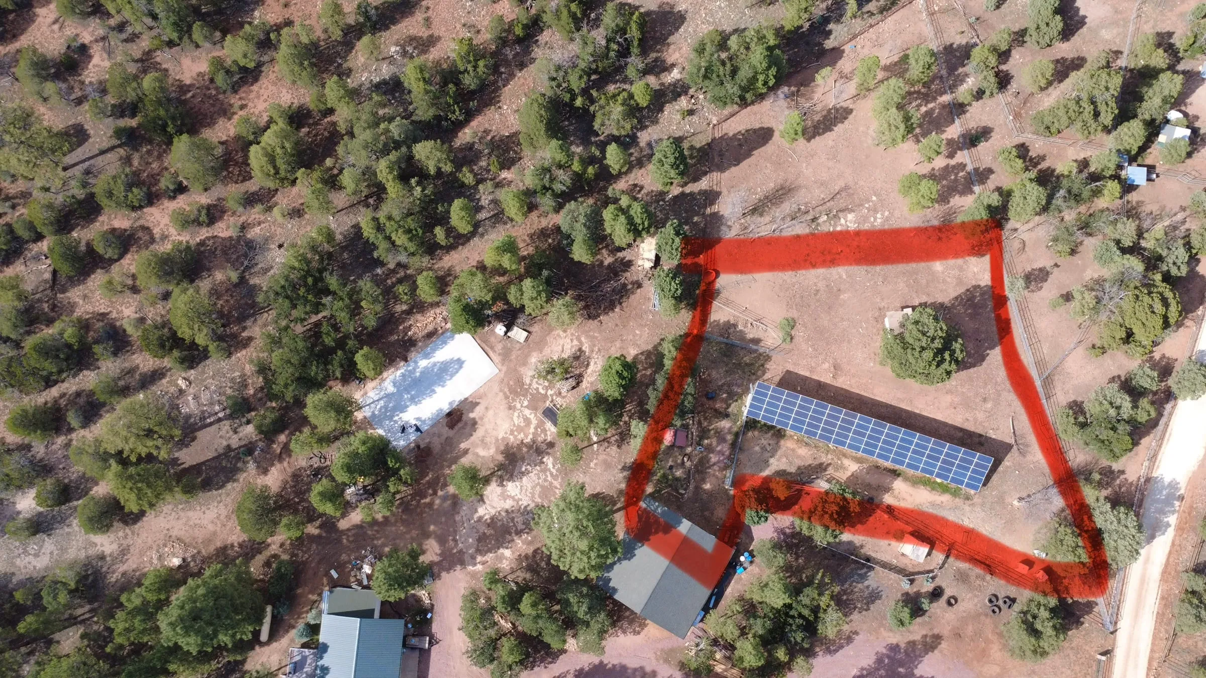 An aerial view of the property with the horse corral outlined in red. The outlined area runs from the barn out to the fence line and takes in open ground, shade trees, and the long bank of solar panels beside the barn.