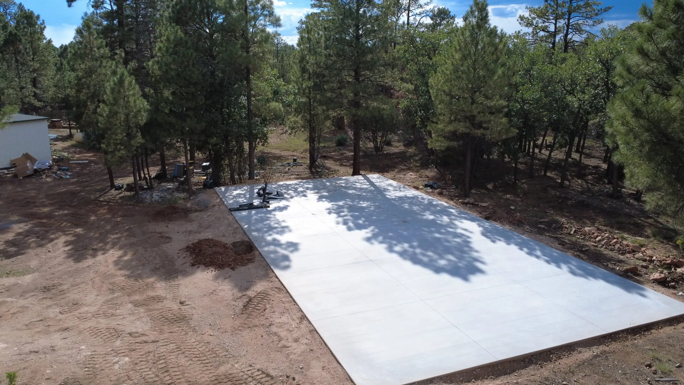 The poured concrete slab for the sport court, seen from the air. It is a full rectangle, edged and finished, in a clearing of ponderosa pines a short walk from the lodge.