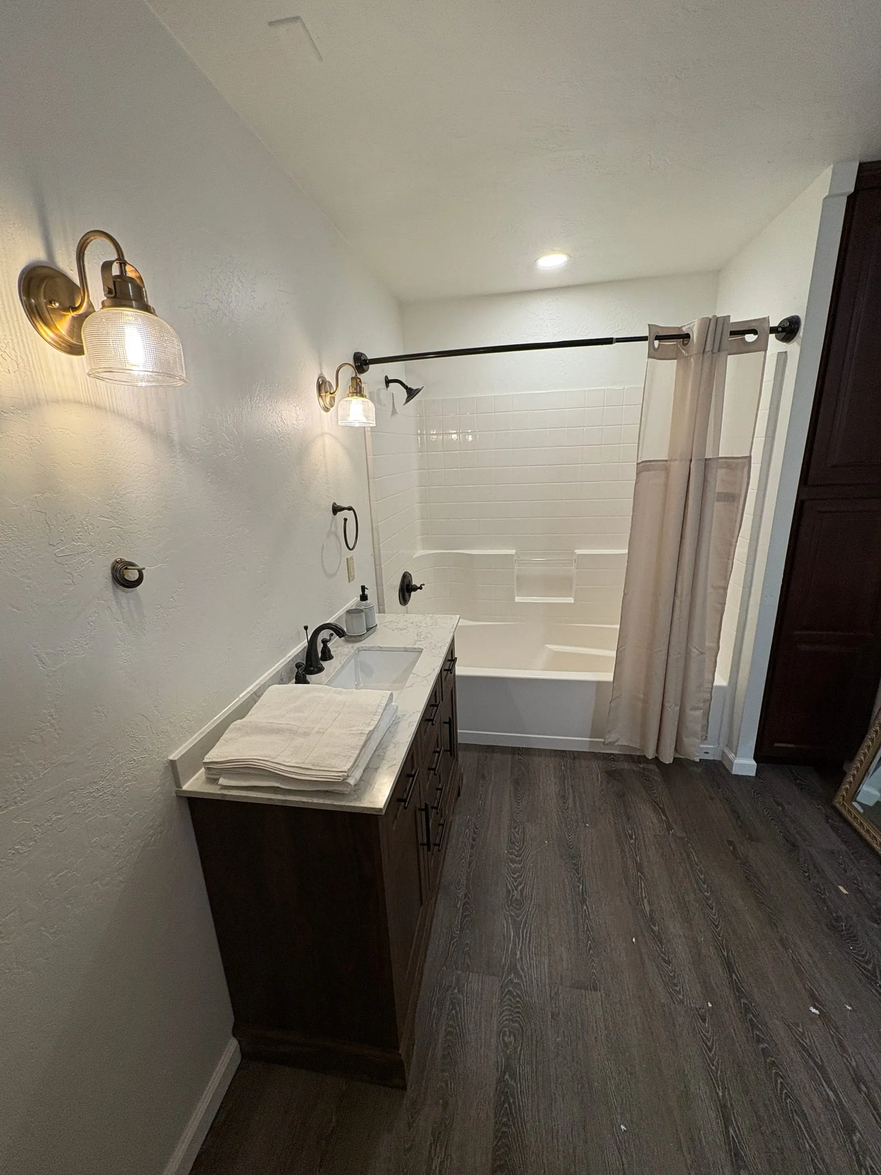 The bathroom off the theater — a tiled walk-in shower beside a dark vanity with a marble top and brass sconces above it.